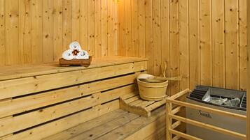 A wooden sauna with benches, a wall-mounted heater, and a sauna table with towels.