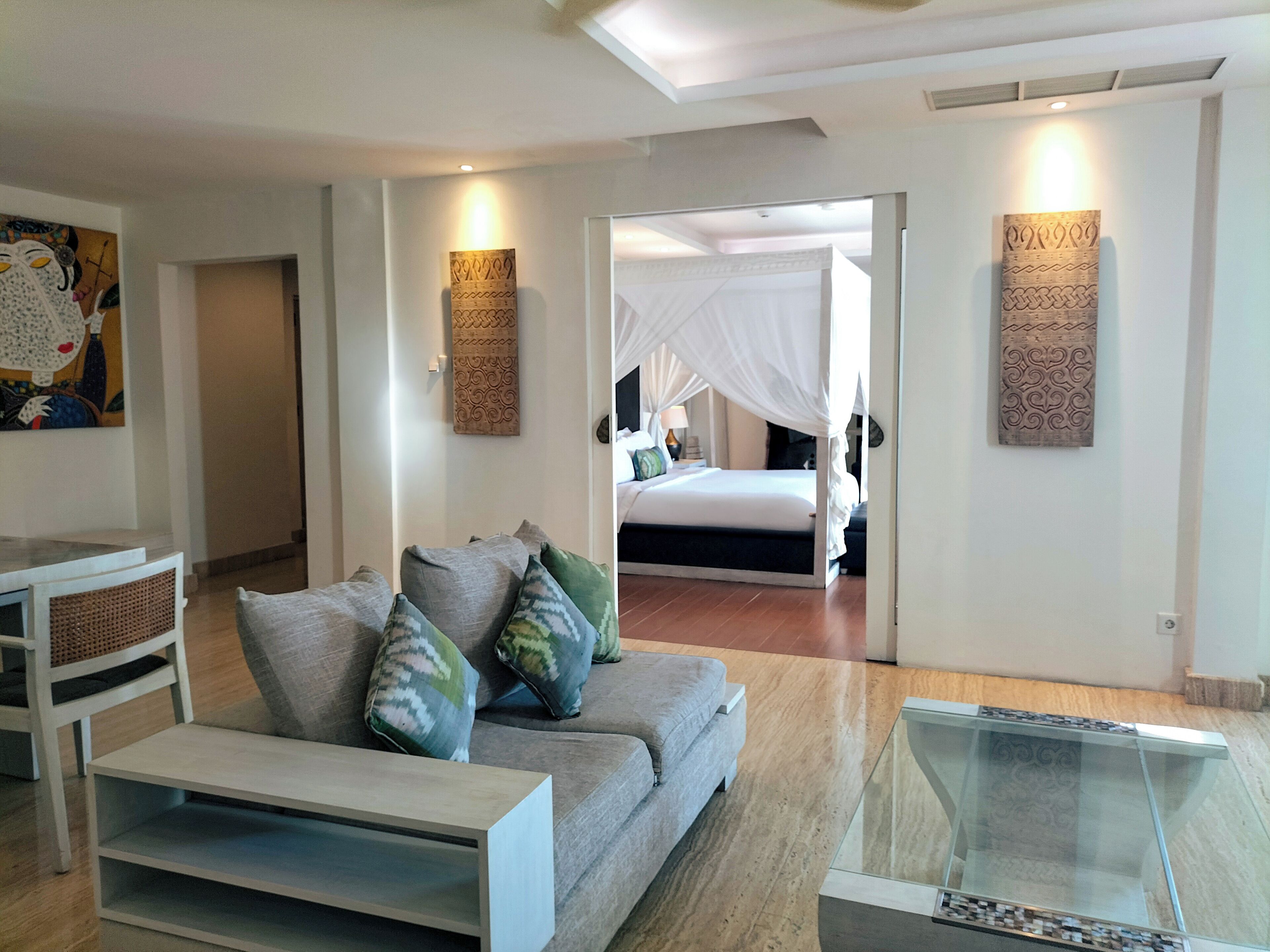 Una sala de estar moderna con un sofá, una mesa de centro de vidrio y una cama con dosel al fondo.