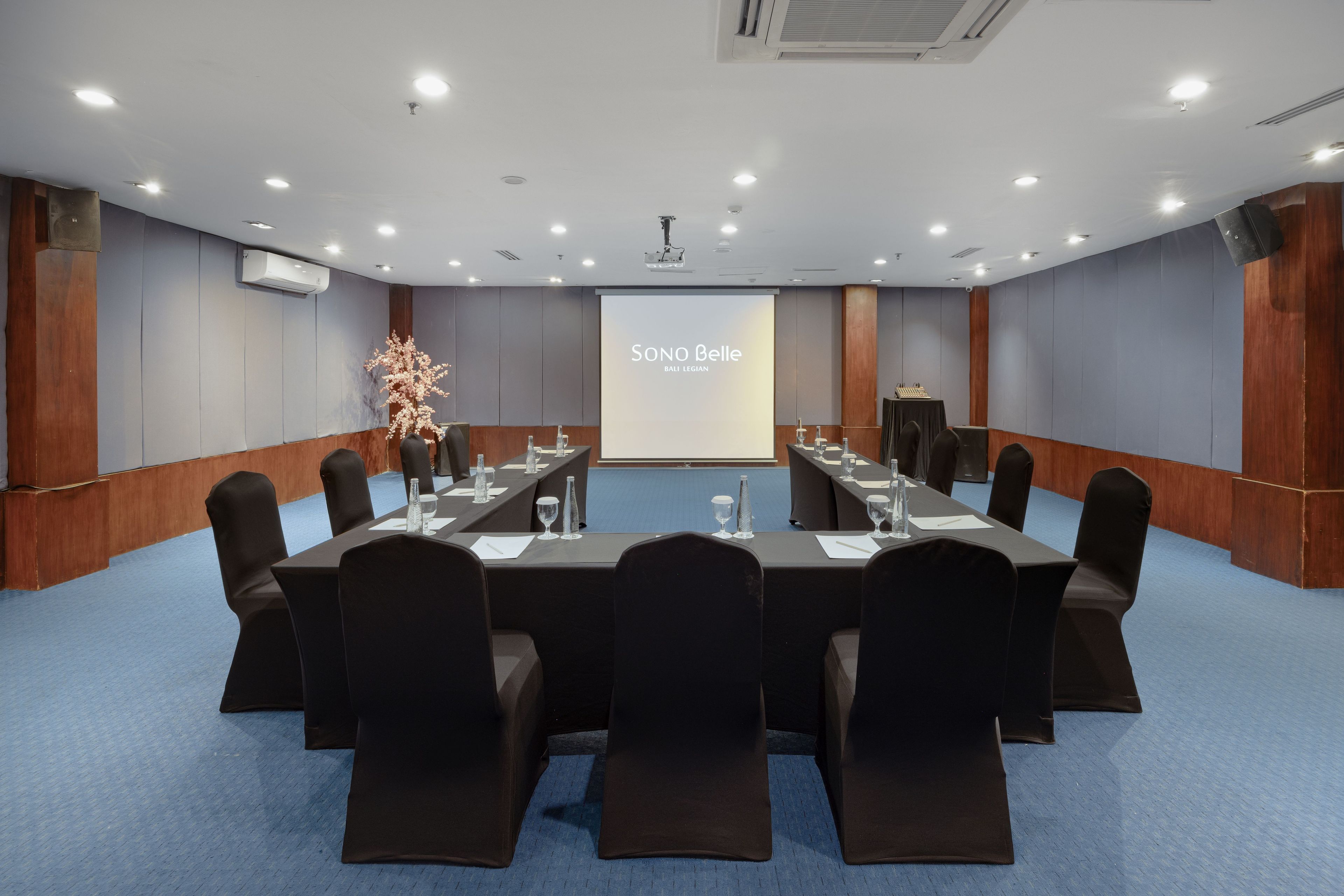 A conference room with a large screen displaying 'Sino Belle' and 'BALI LEGIAN'.