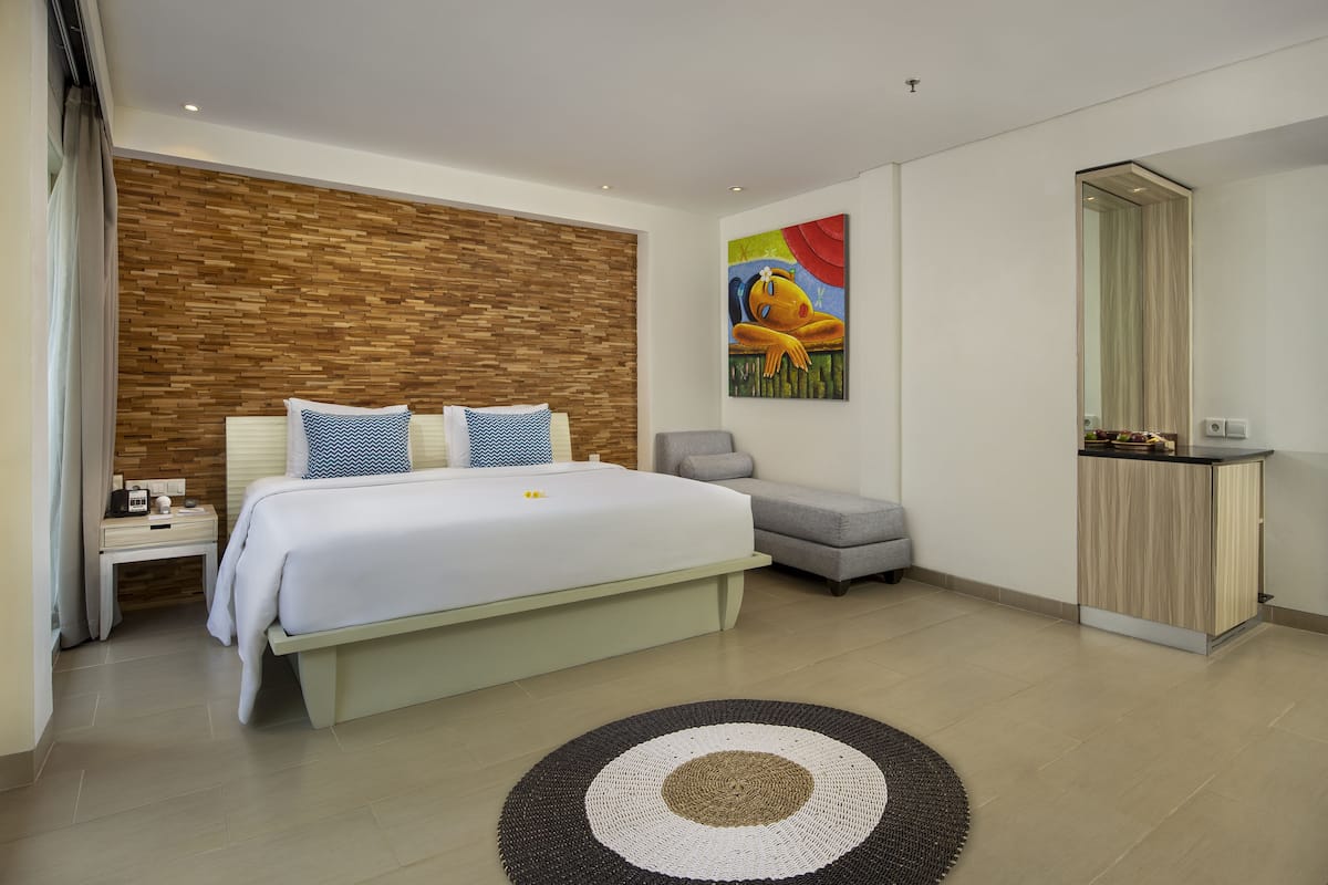 A modern bedroom with a large bed, a wooden accent wall, a gray armchair, and a painting.