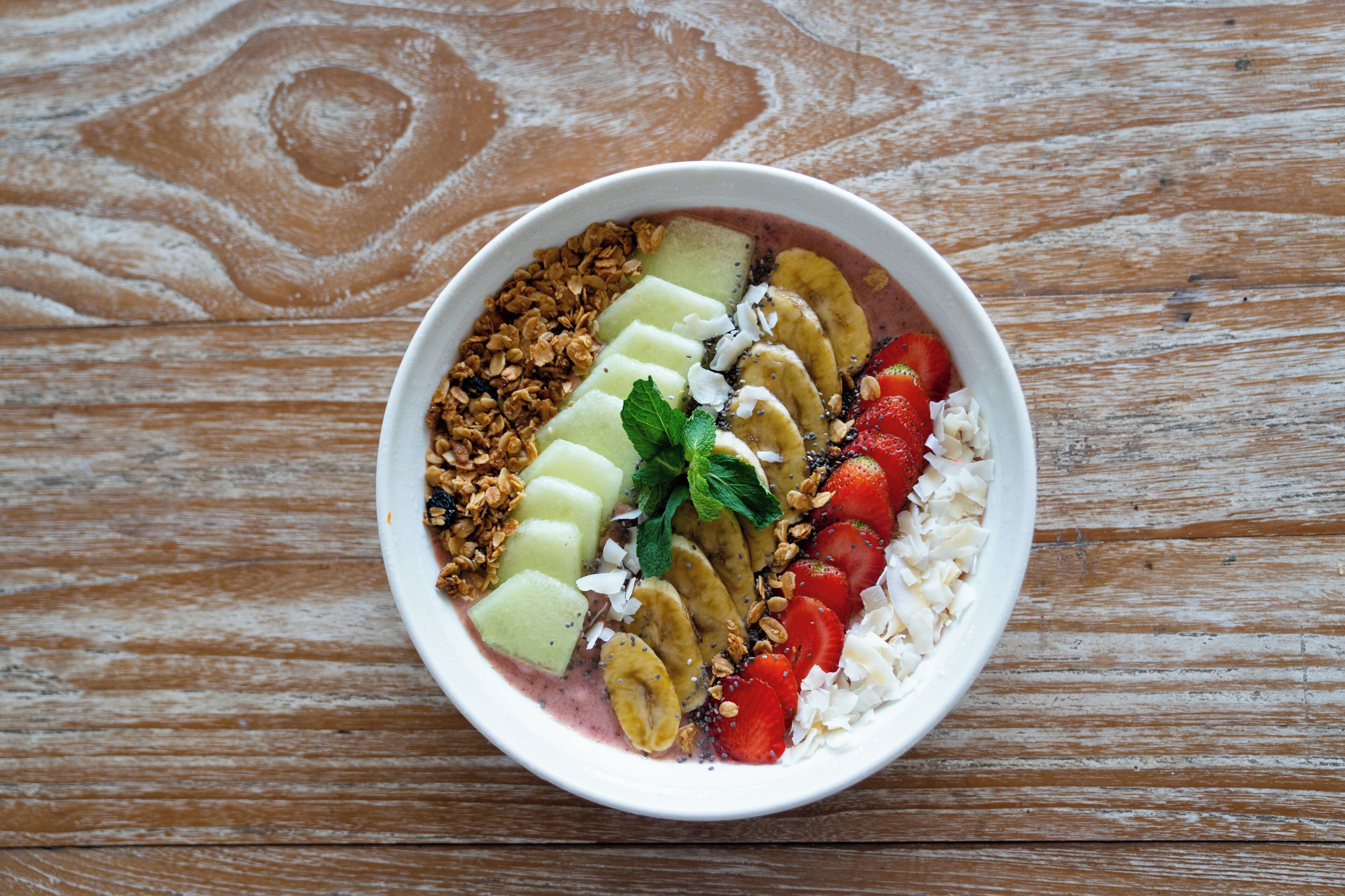 Eine Schüssel mit Obst und Granola auf einer Holztischplatte.