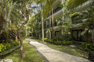 A pathway leading to a building with multiple balconies, surrounded by lush greenery and palm trees.