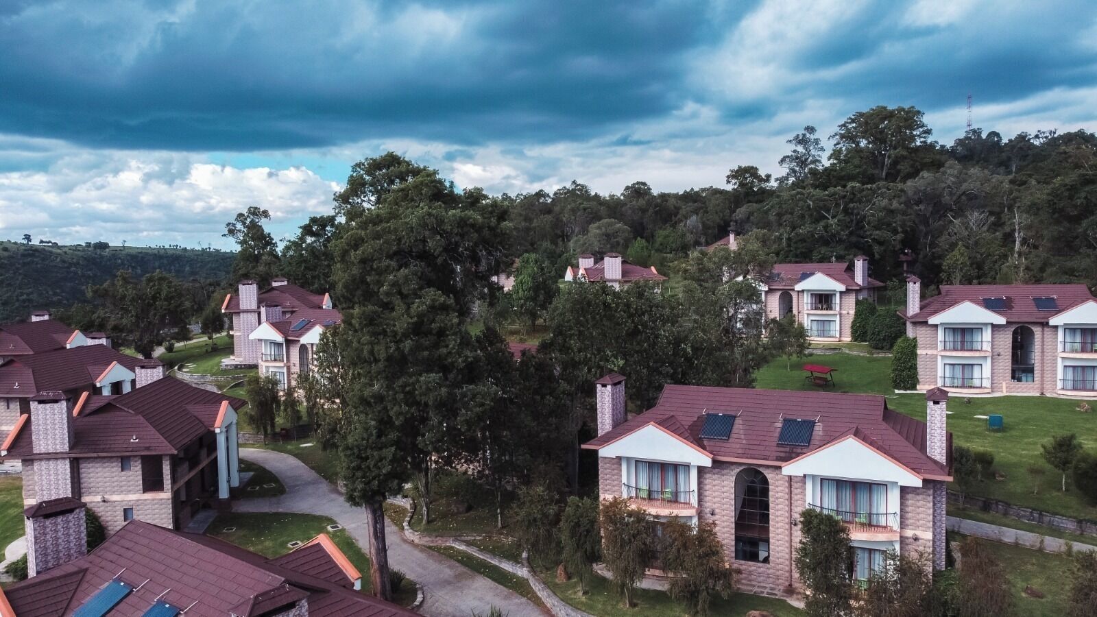 A residential area with multiple houses, each featuring a distinct architectural style, surrounded by lush greenery and a hilly landscape.