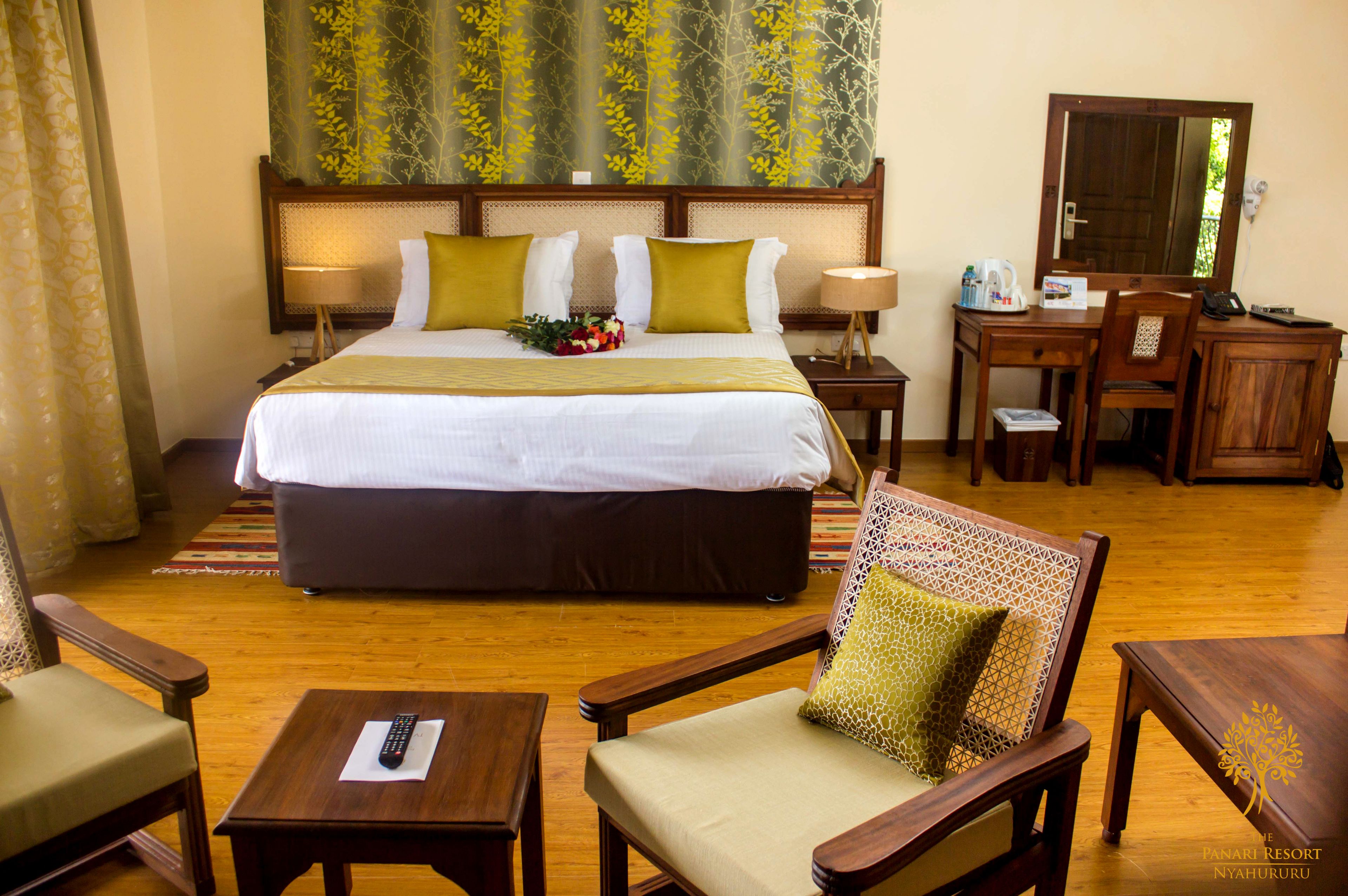A hotel room with a large bed, two bedside tables, a desk with a chair, a small table with a remote control, and a decorative wall hanging.