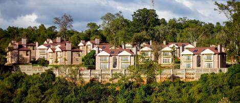 Ein Resort mit mehreren Gebäuden, jedes mit einem eigenen architektonischen Stil, roten Dächern und weißem Zierdekor. Üppiges Grün und Bäume umgeben das Resort und bilden eine natürliche Kulisse.