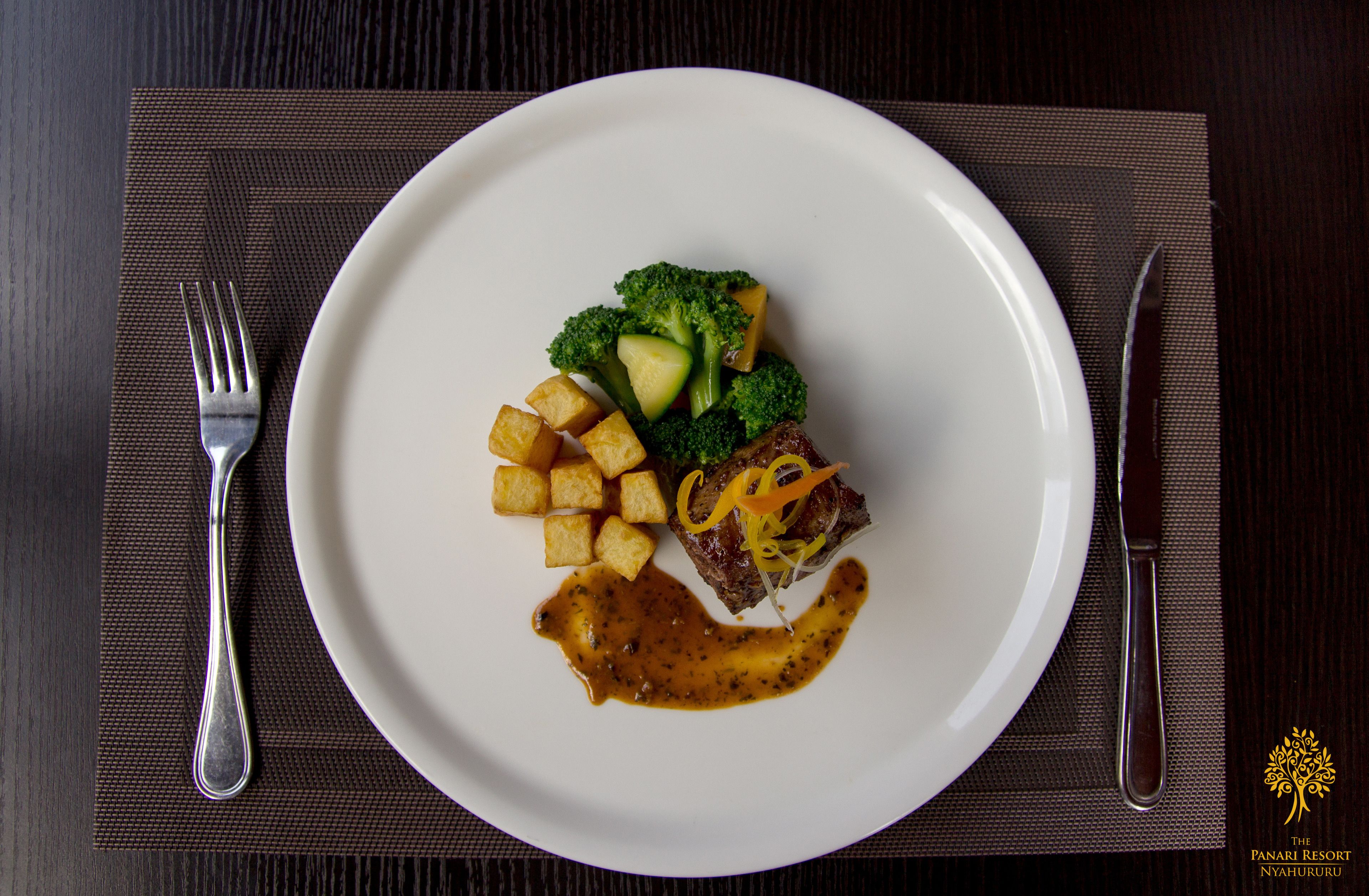 A white plate with a steak, broccoli, and a sauce on a dark placemat.