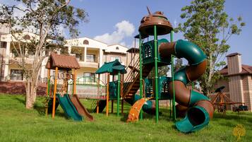 Kids can play on the playground's slides and climbing areas in a lush green space.