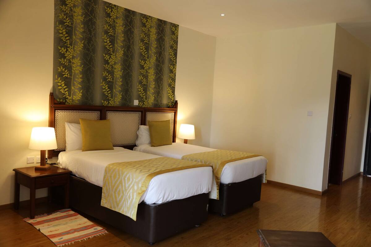 A hotel room with two beds, a large window with a view, and a wooden floor.