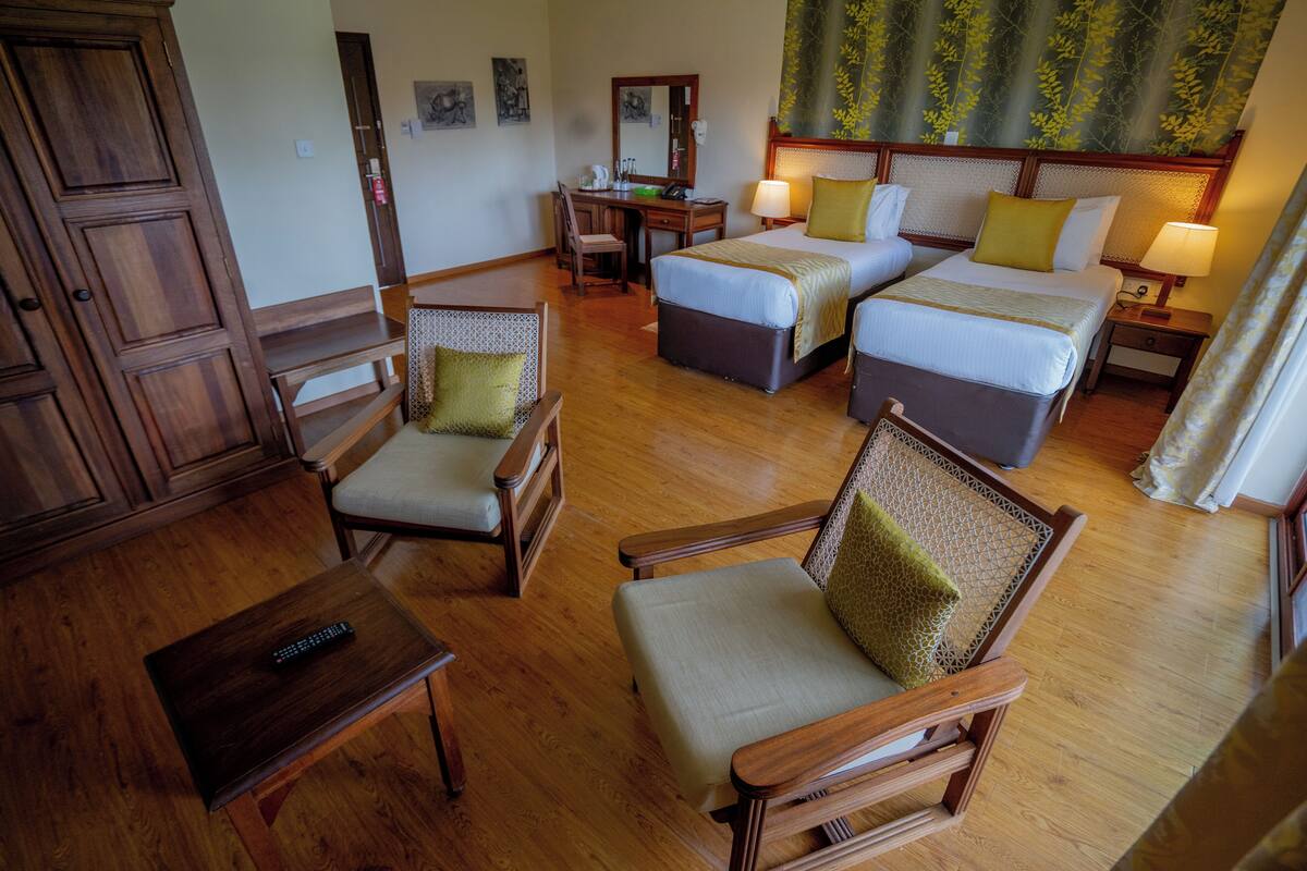 A hotel room with a wooden floor, two beds, a desk, a chair, and a wardrobe.