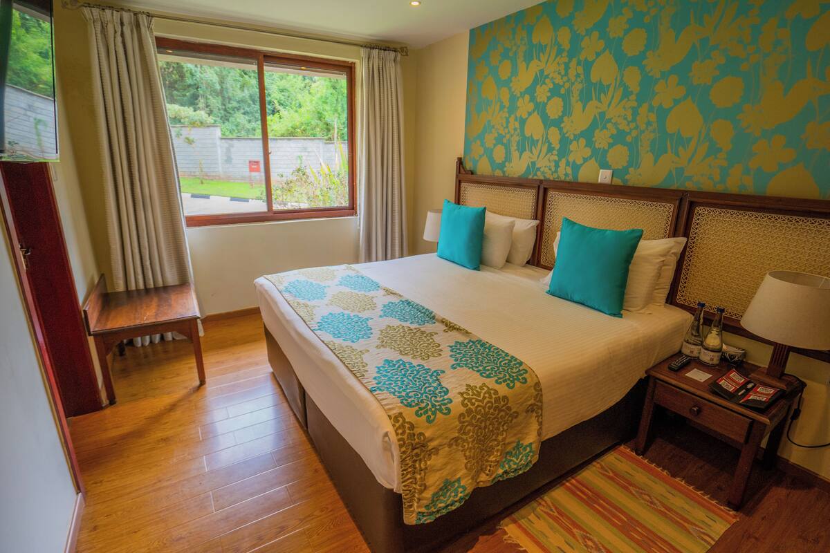A hotel room with a large bed, a desk, a nightstand, and a window with curtains.