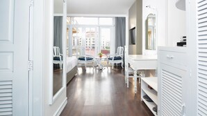 Een hotelkamer met een groot raam, een witte kaptafel, een stoel, een kleine tafel met een plant en een garderobe.