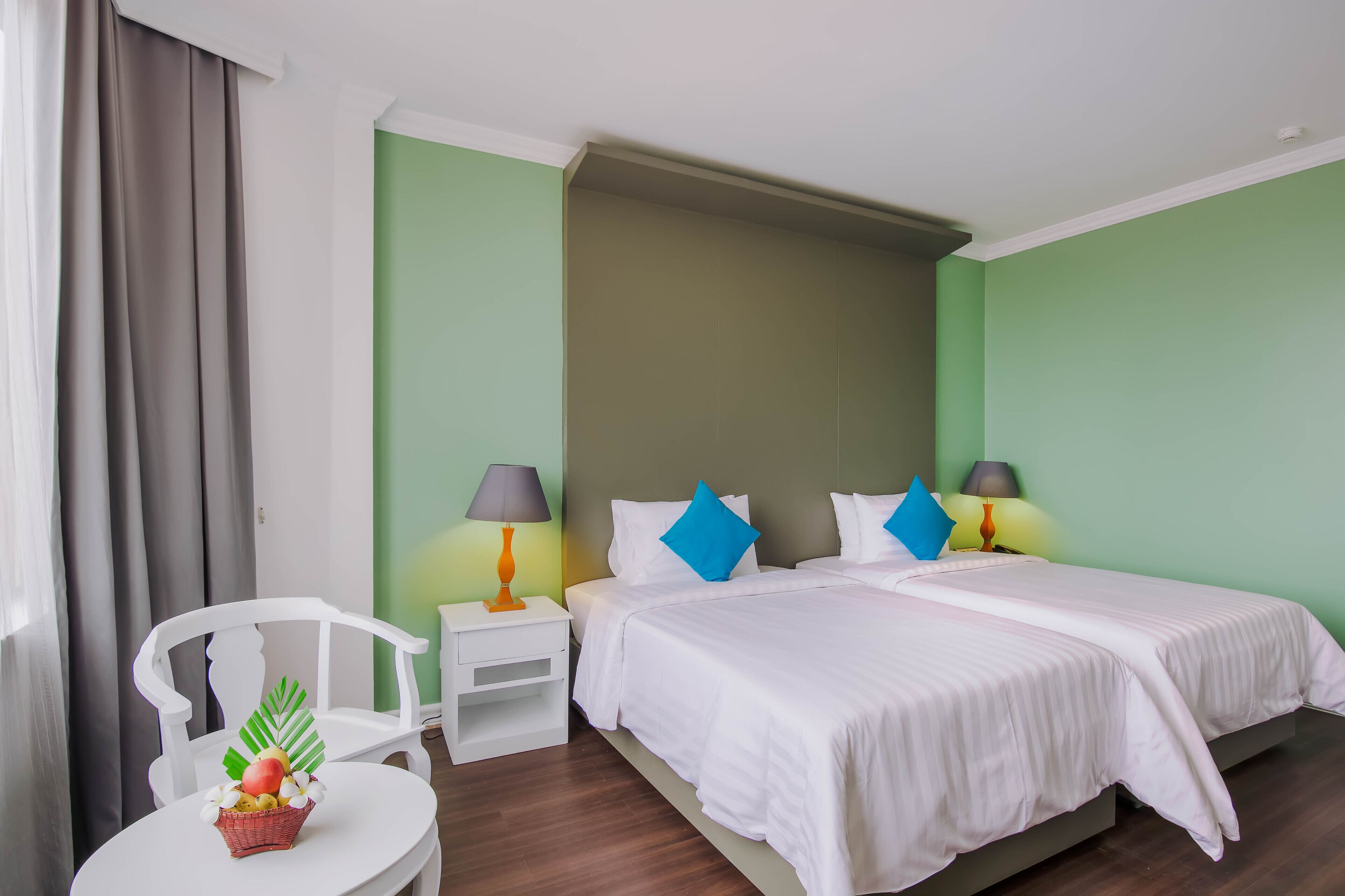 A hotel room with two beds, a small table with a lamp, a chair, and a decorative basket.