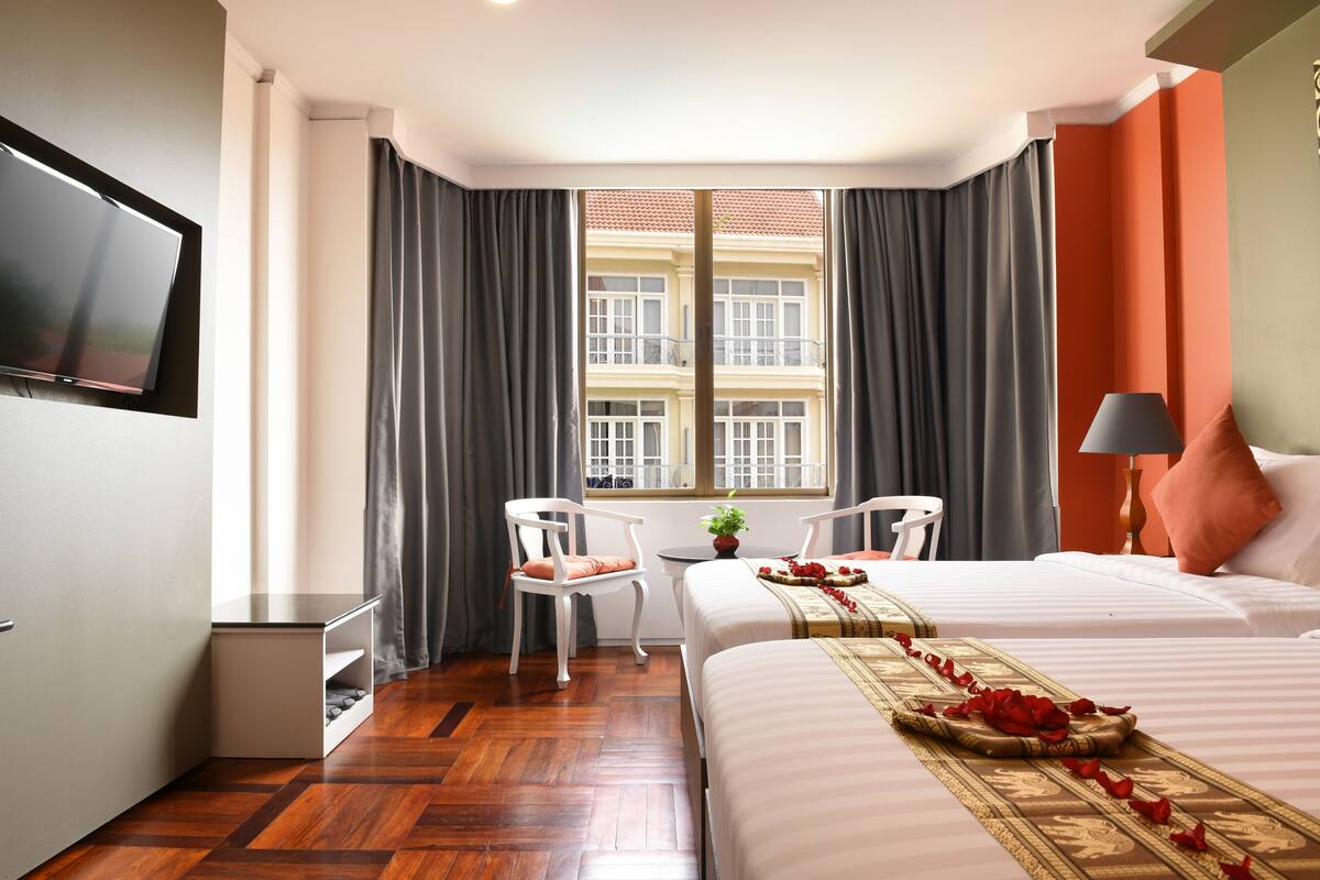 Ein Hotelzimmer mit Bett, Fernseher, Schreibtisch mit Stuhl und Fenster mit Vorhängen.