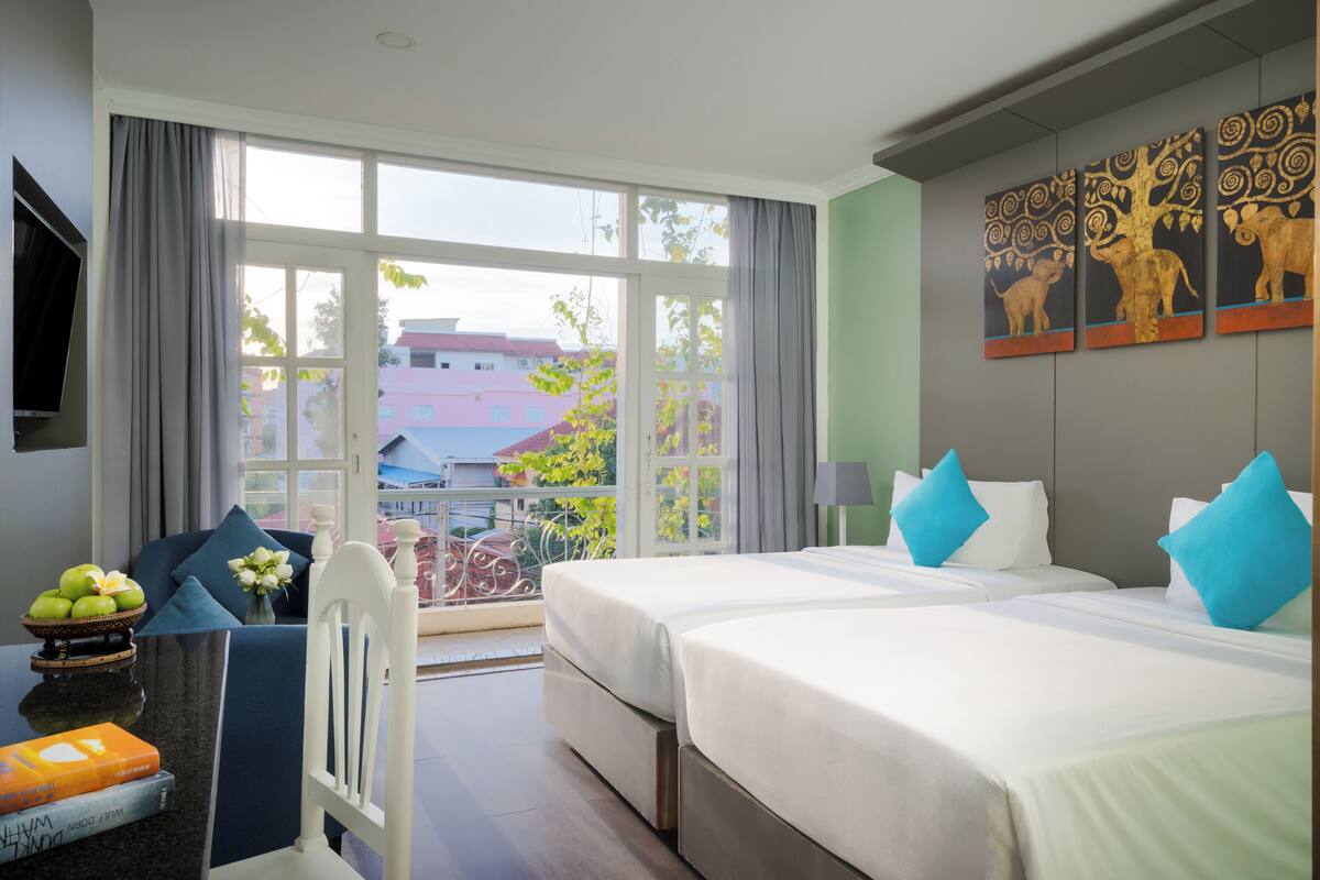 Ein Hotelzimmer mit zwei Betten, einem Balkon, einem Fernseher und einem Bild an der Wand.