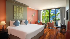 Een hotelkamer met een groot bed, een bureau, een stoel en een balkon met uitzicht op palmbomen.