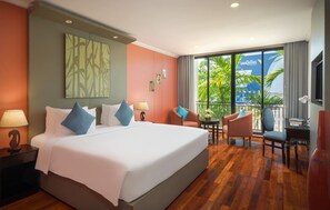 A hotel room with a large bed, a desk, a chair, and a balcony with a view of palm trees.