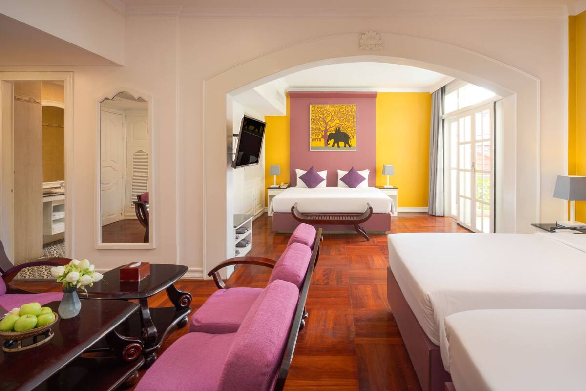 Ein Hotelzimmer mit Bett, Sofa, Esstisch mit Äpfeln, Spiegel und Fernseher.