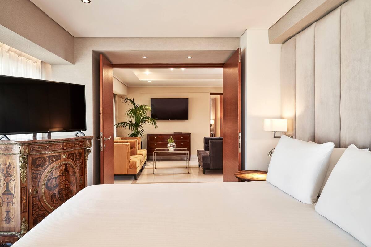 Une chambre d’hôtel avec un grand lit, un téléviseur à écran plat, une armoire en bois, un canapé, une table basse et un téléviseur fixé au mur.