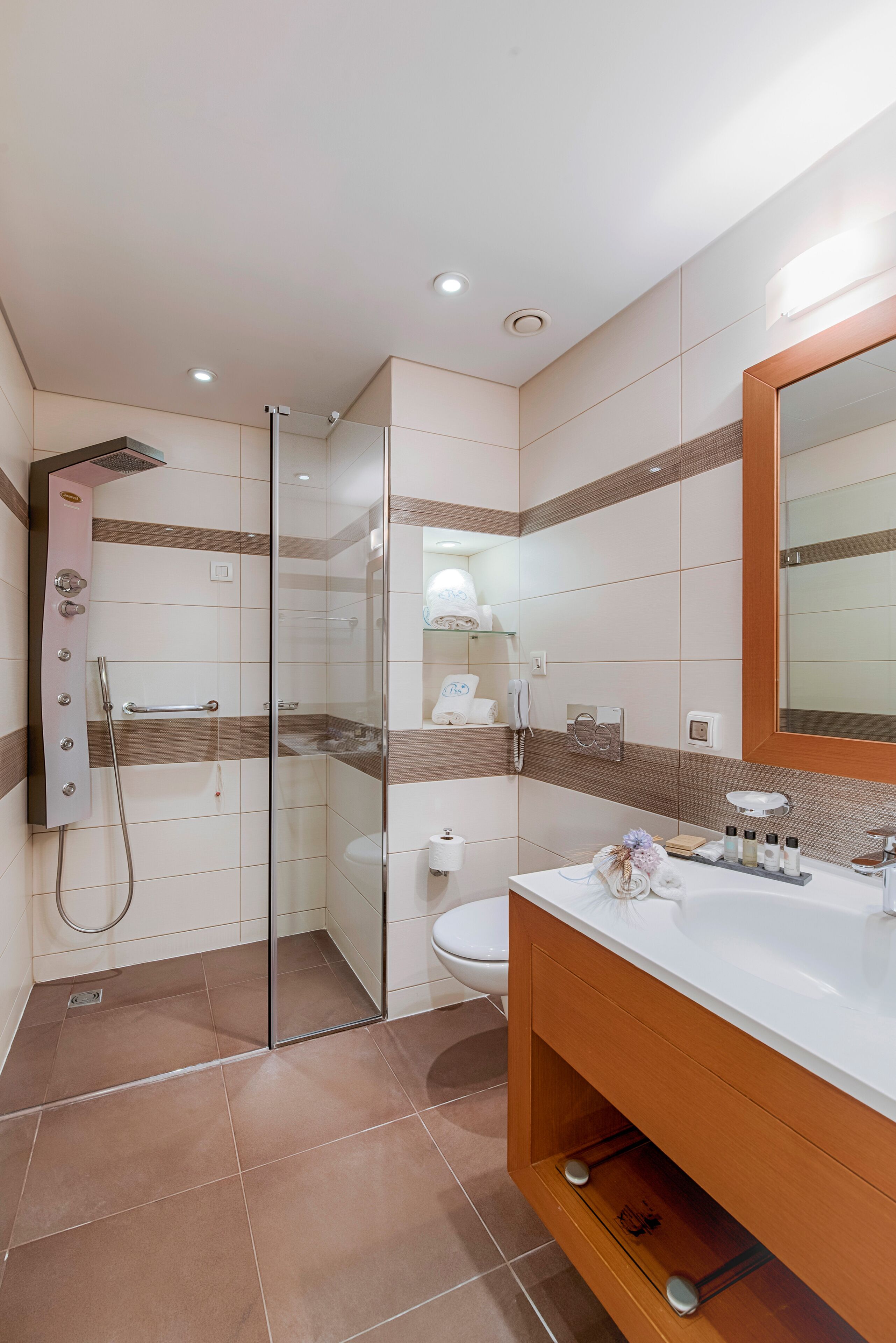 Un baño moderno con ducha envuelta en vidrio, un lavamanos blanco sobre un mueble de madera y un espejo grande.