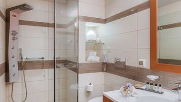 Un baño moderno con ducha envuelta en vidrio, un lavamanos blanco sobre un mueble de madera y un espejo grande.