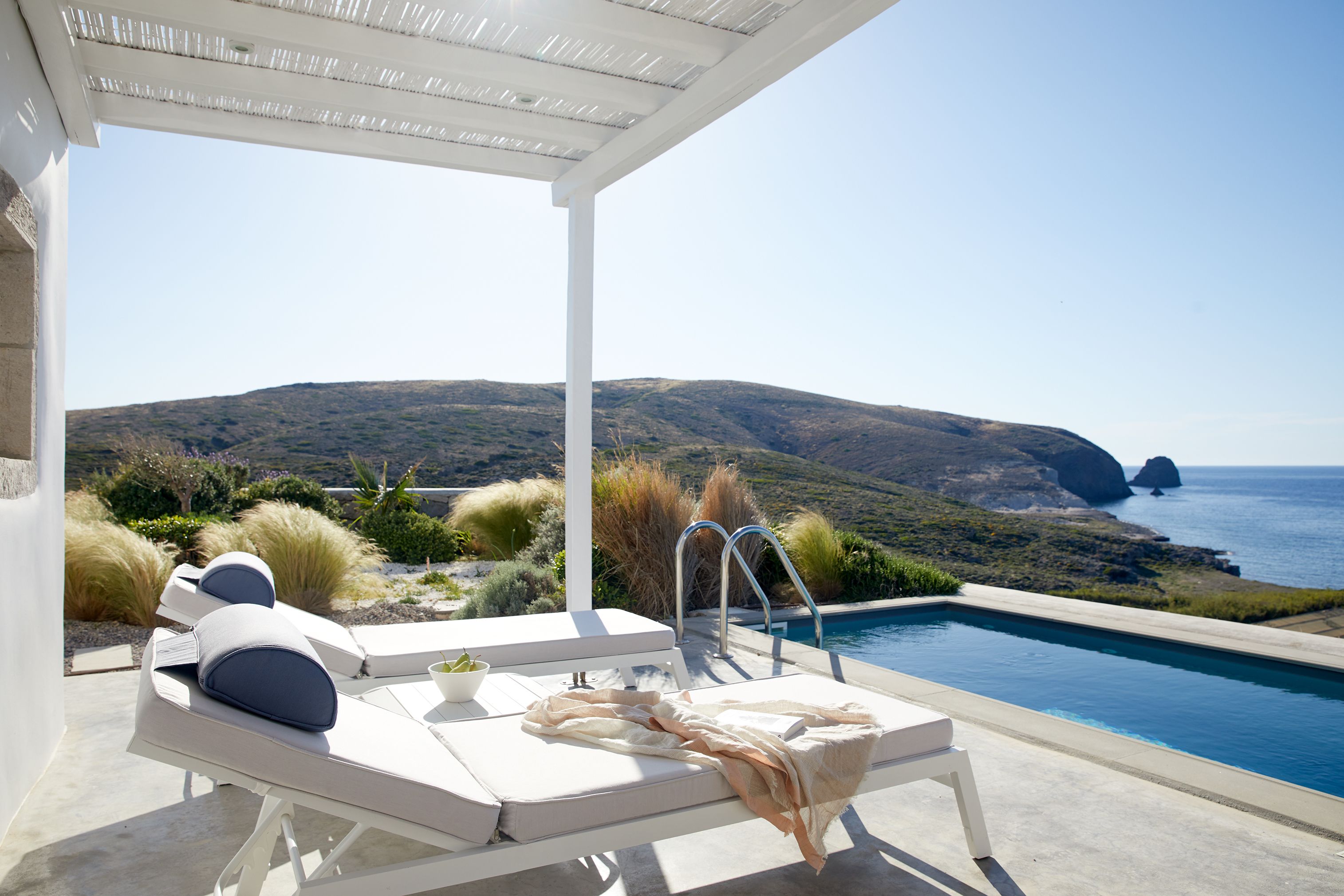 Un espace aménagé au bord de la piscine, avec des chaises longues et une vue sur la mer et les collines.