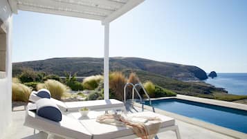 Zona junto a la piscina con sillones de descanso y vistas al mar y las colinas.