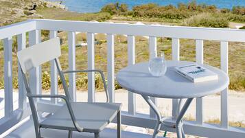 A white metal chair and table on a balcony with a clear view of the ocean and rocky coastline.