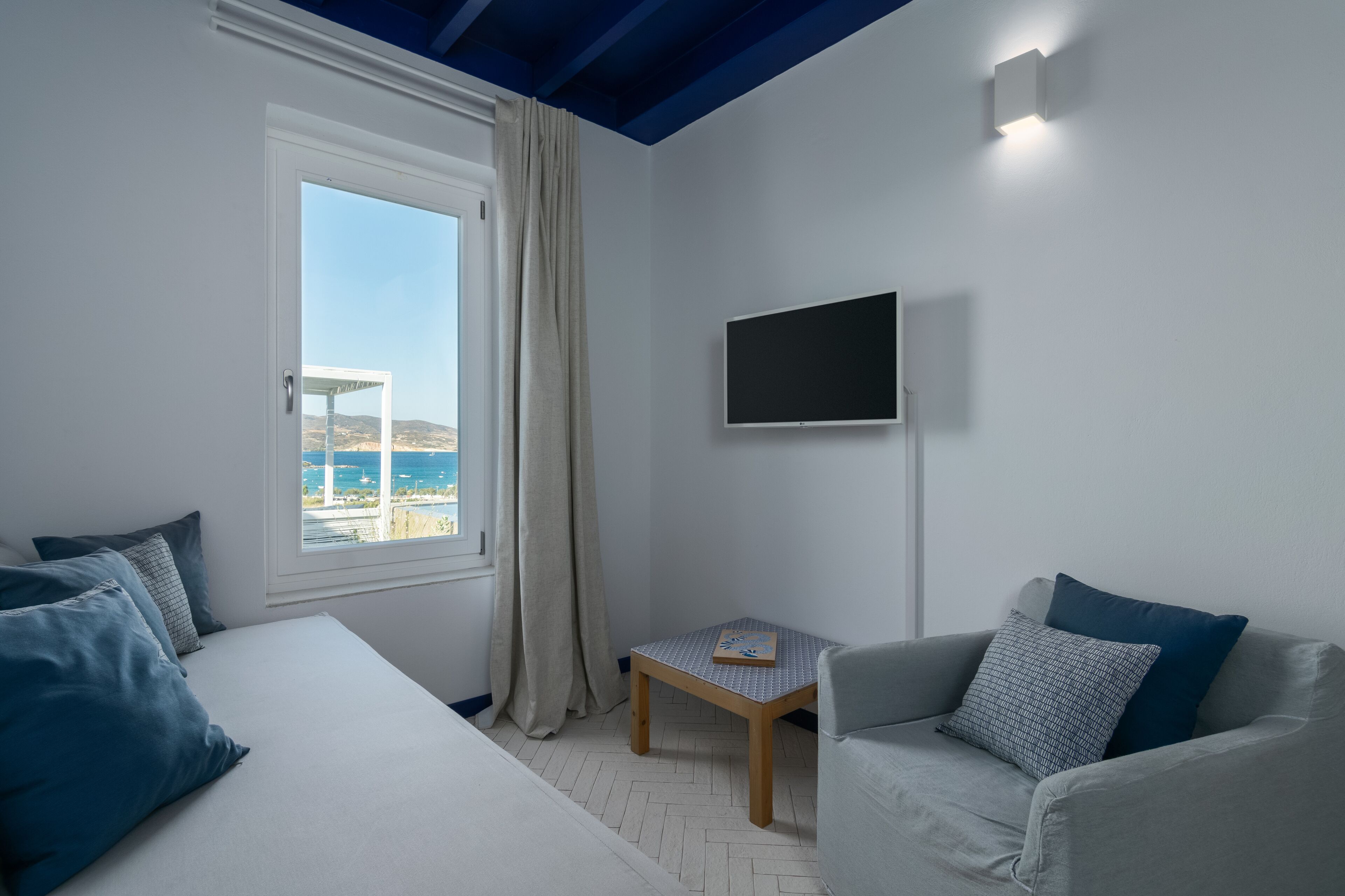 Une chambre avec un lit, une petite table, un téléviseur et une vue sur la mer.