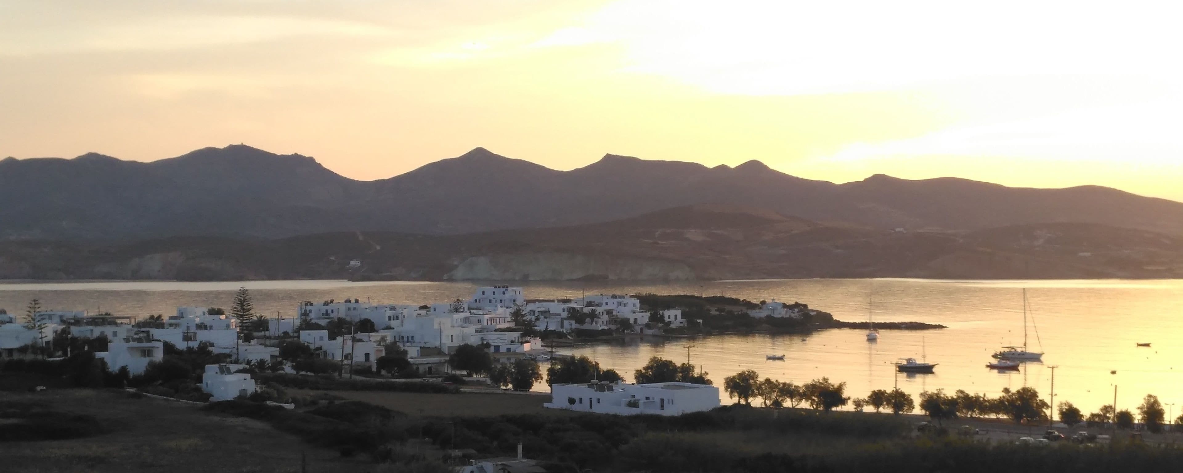 Un pueblo costero con edificios blancos, una masa de agua y montañas al fondo.