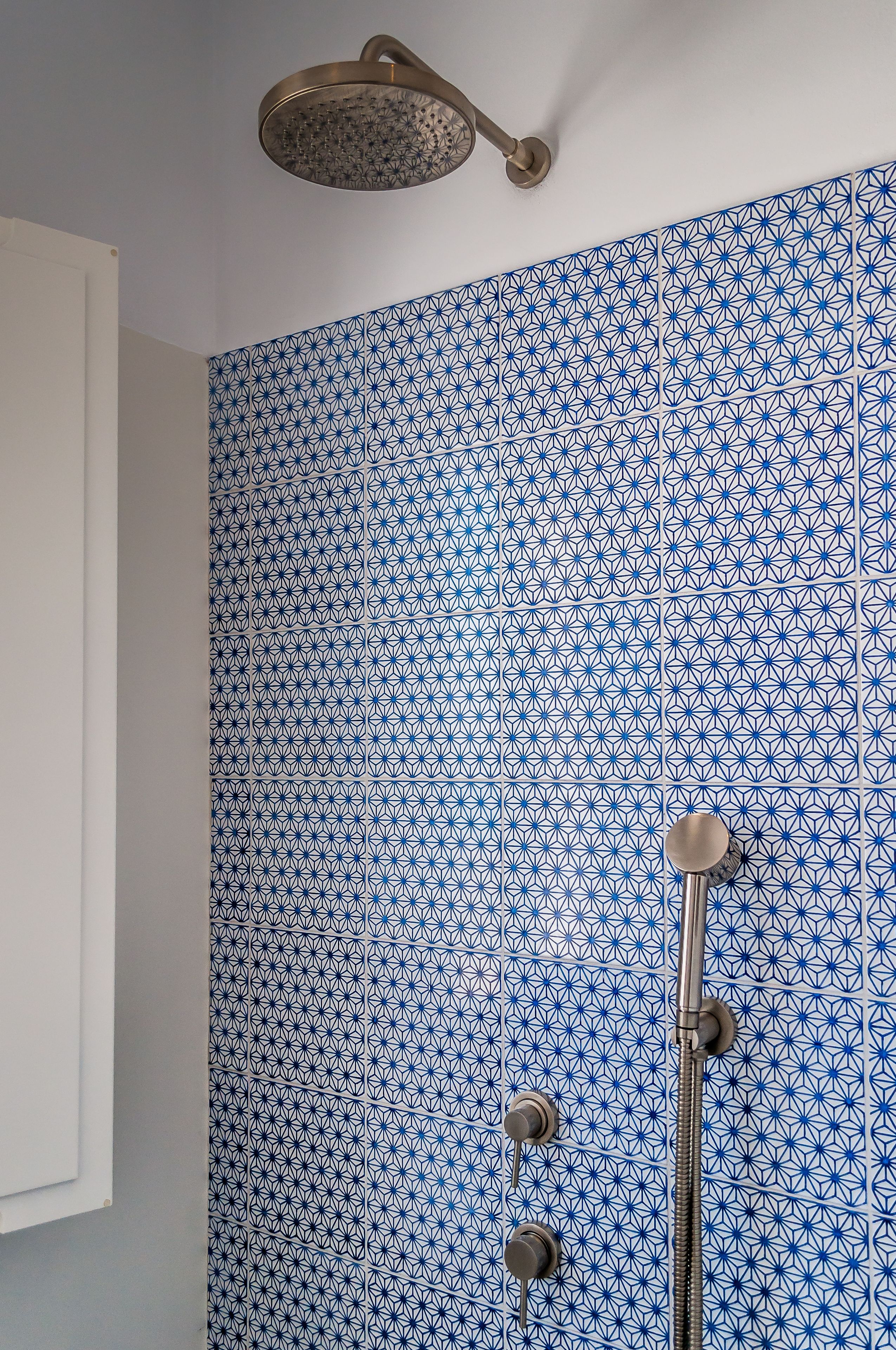 A bathroom with blue patterned tiles, a showerhead, and a handheld shower attachment.