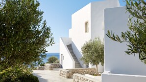 Un moderno edificio blanco con una escalera que lleva a una puerta, rodeado de follaje y vista al mar.