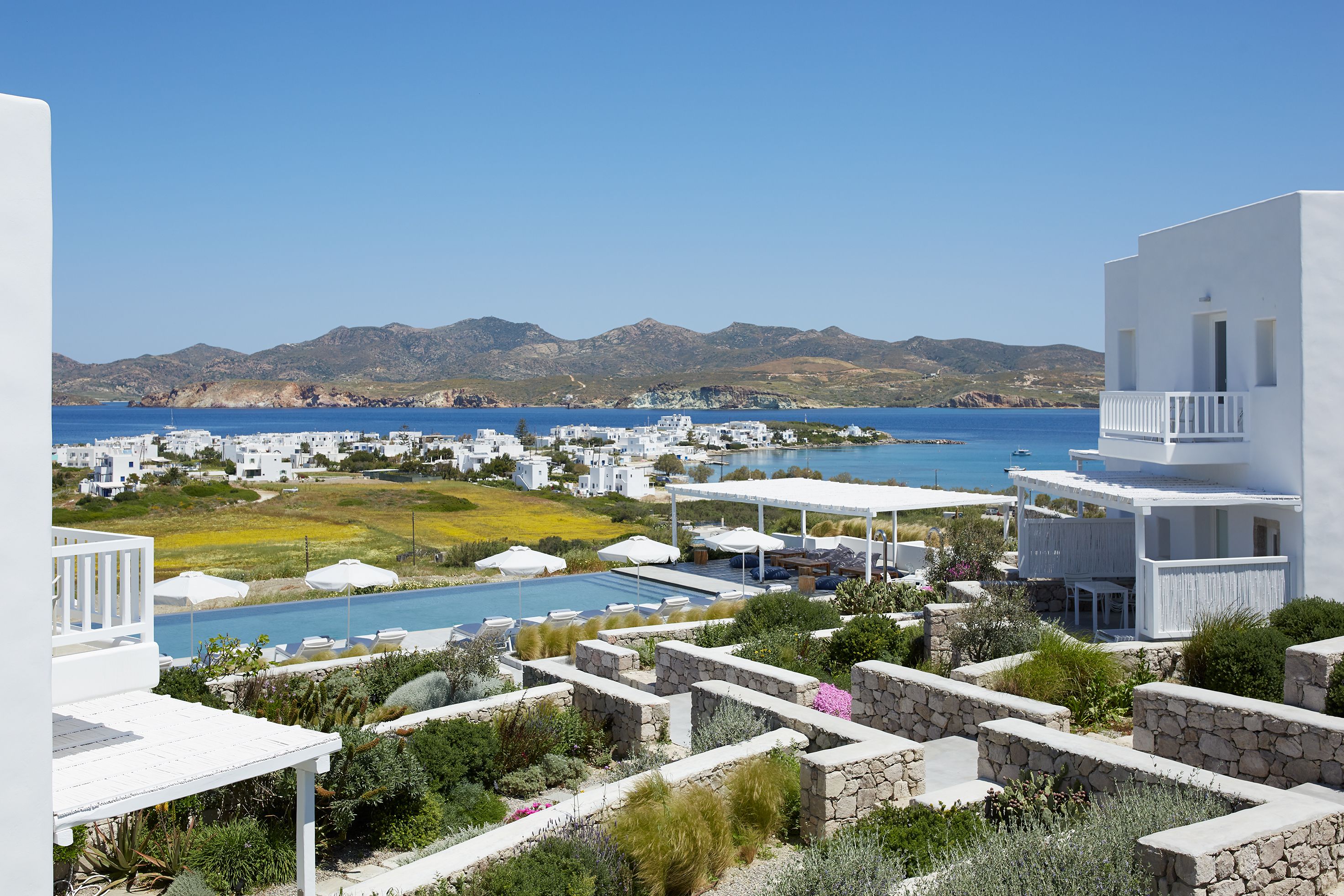 Un complejo turístico frente al mar con edificios blancos, una piscina y vistas al océano y las montañas.