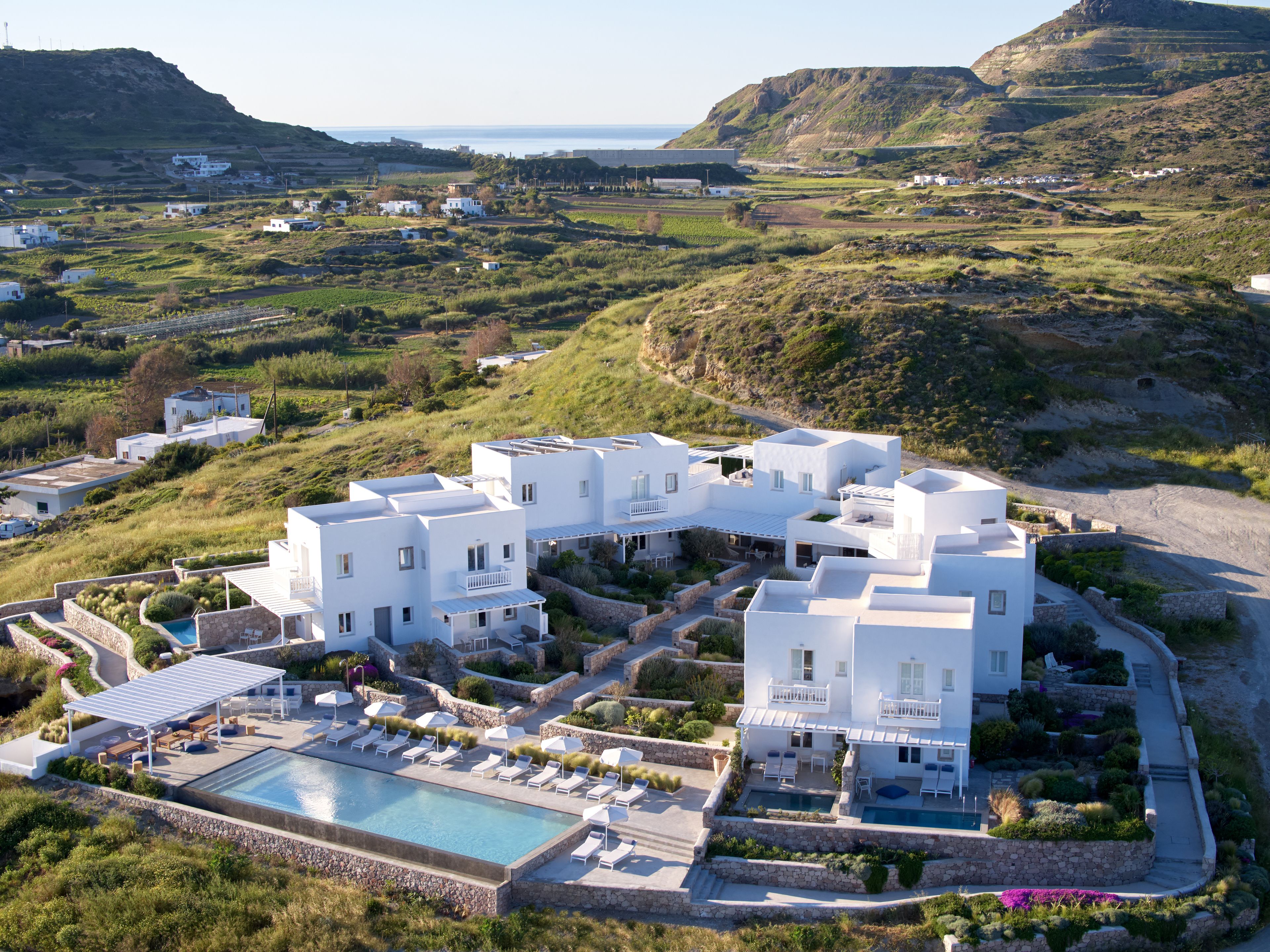 A white, modern villa with a pool, surrounded by lush greenery and hills.