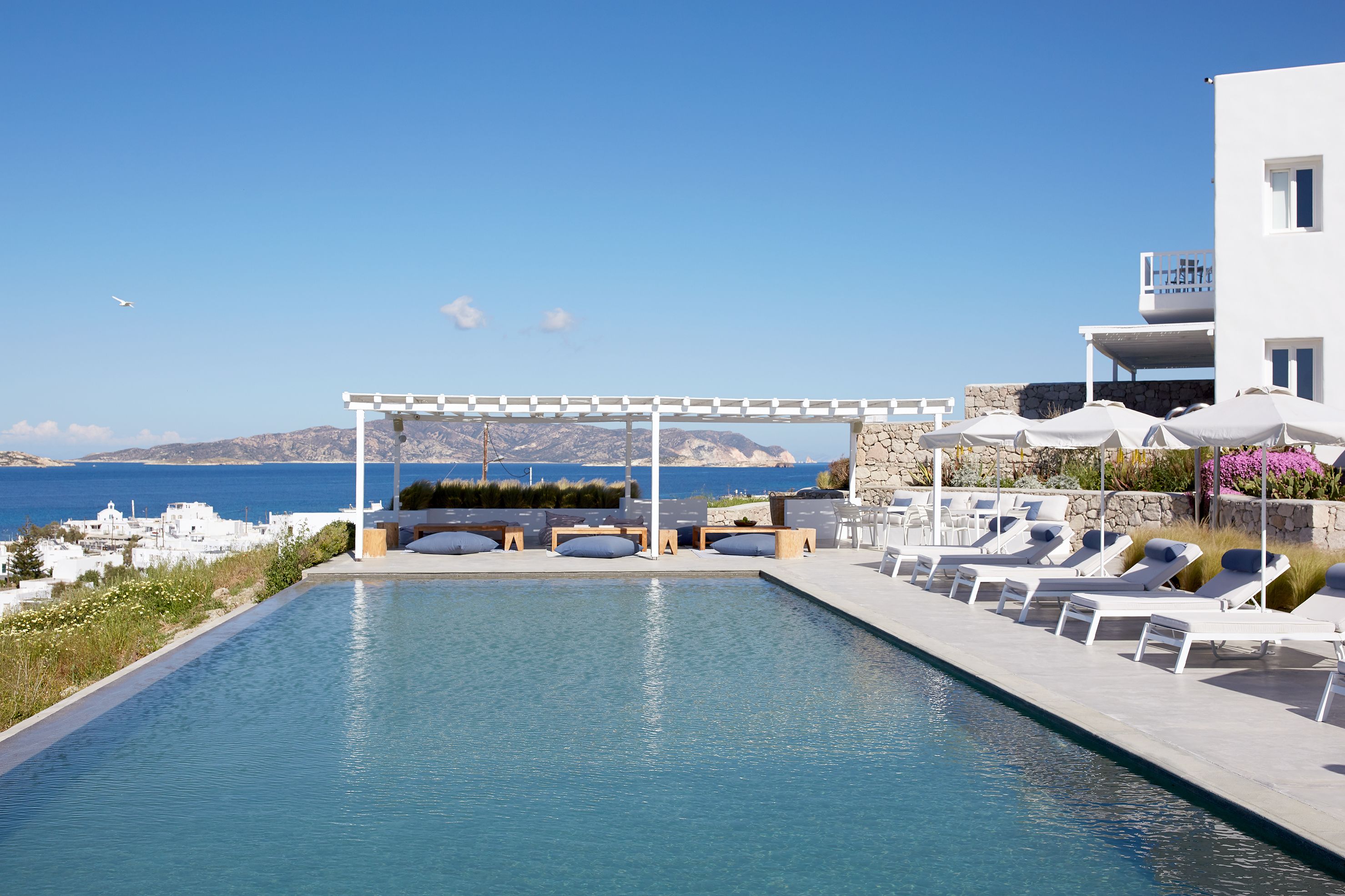 A pool area with lounge chairs and a pergola overlooking the sea.