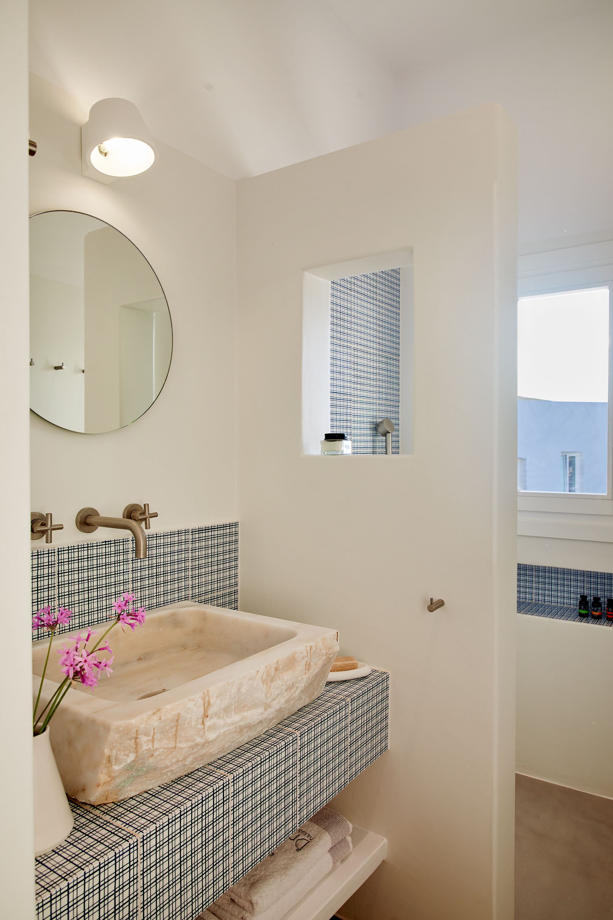 A bathroom with a large, freestanding bathtub, a round mirror, and a small window with a grid pattern.