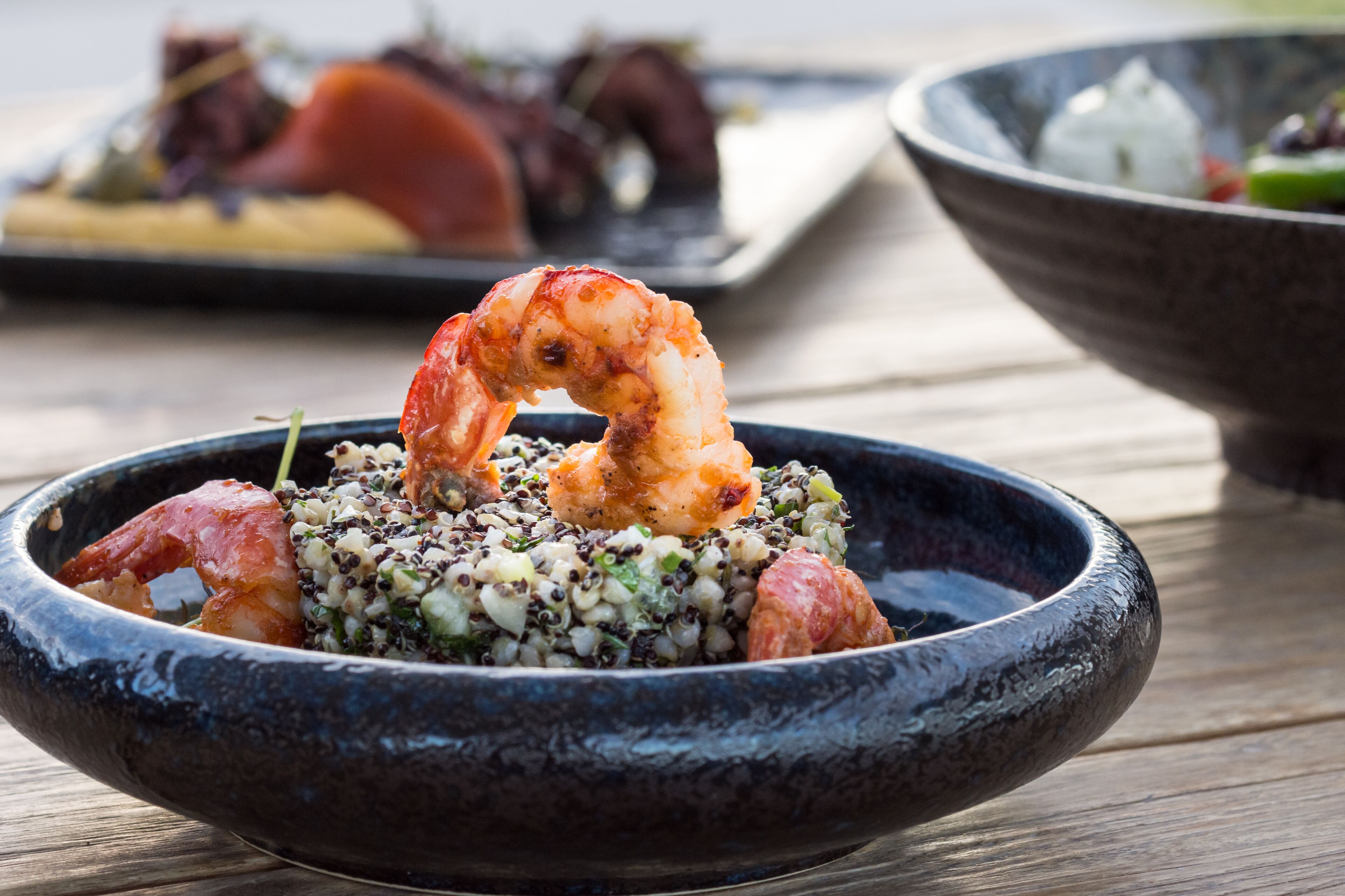 Una ciotola di cibo con gamberi e cereali, probabilmente quinoa, su un tavolo di legno.