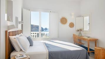 A bedroom with a bed, a desk, and a chair. There is a window with a view of the sea.