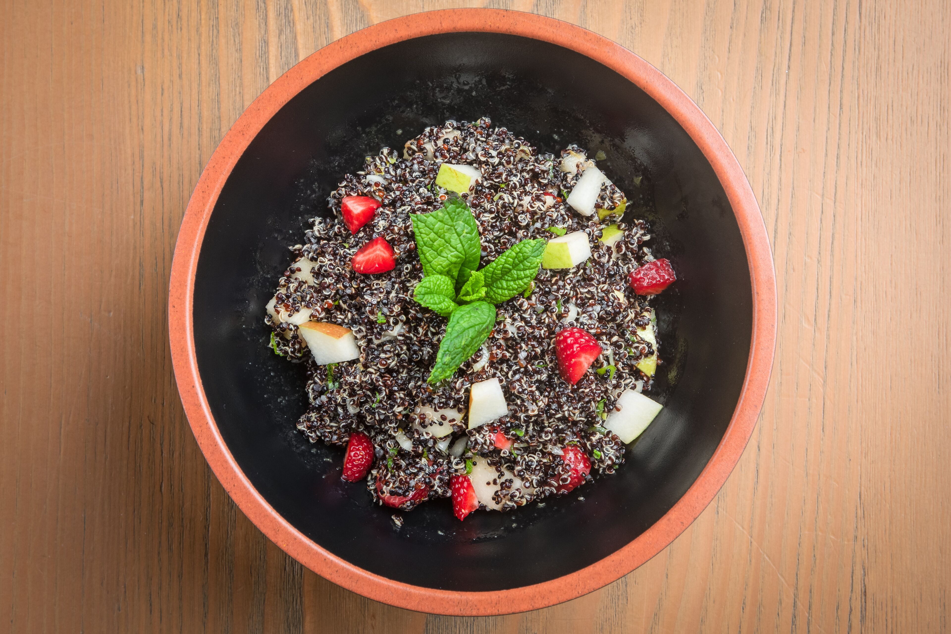 Un tazón de ensalada de quinoa con fresas y menta sobre una mesa de madera.