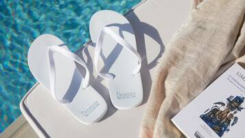 A pair of white flip-flops with the 'breeze' logo on a white lounge chair by a pool.