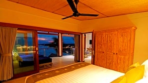 A bedroom with a bed, a ceiling fan, a view through a glass door to the outside, and a wooden wardrobe. - Lembongan Sanctuary Villas (Lembongan Island)