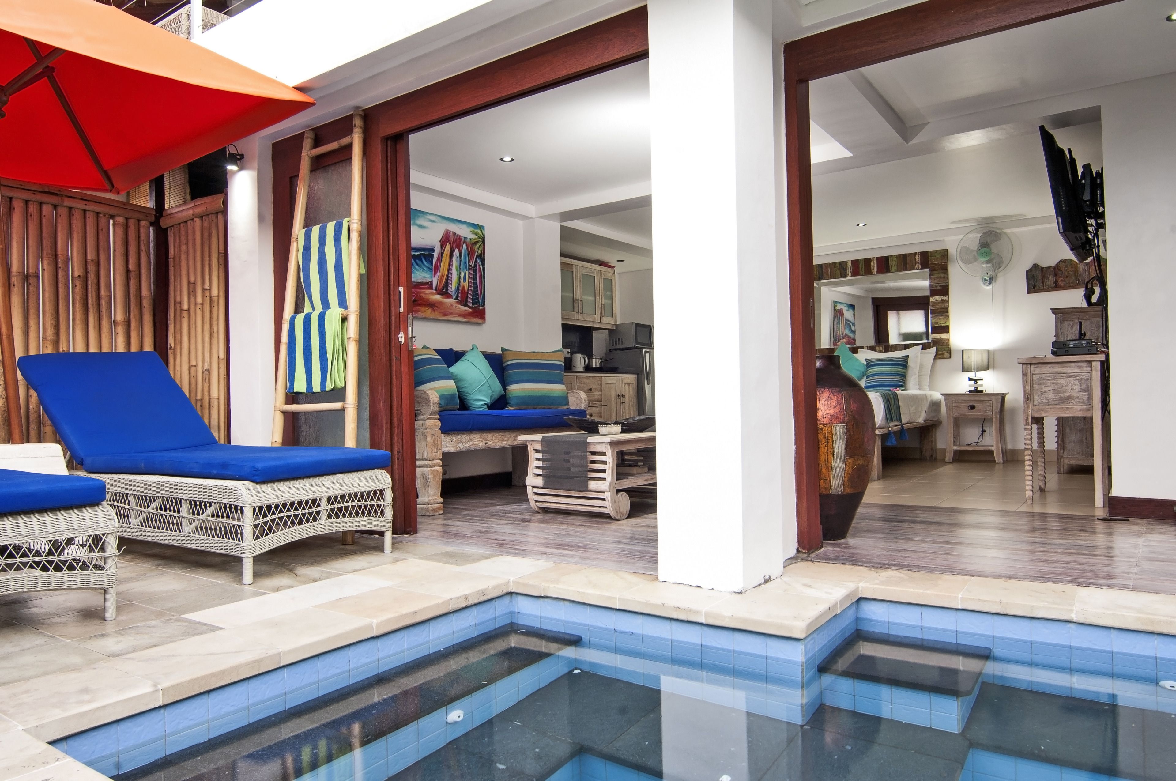 A pool area with lounge chairs, a dining area with a table and chairs, and a kitchen in the background.