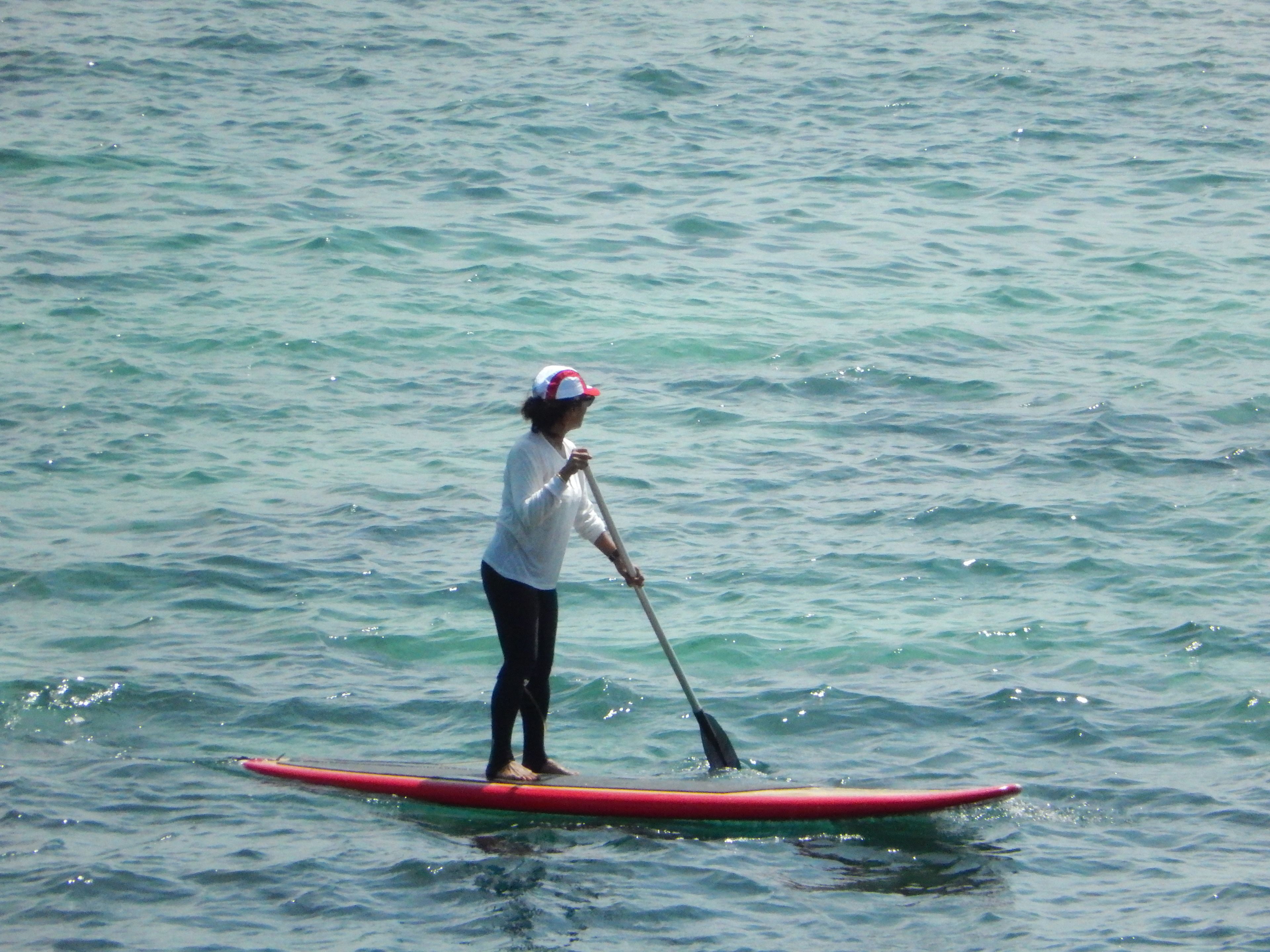 A person standing on a red paddleboard in the water.