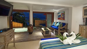 A modern hotel room with a large bed, a sofa, a TV, a wooden coffee table, and a view of a pool and palm trees. - Lembongan Sanctuary Villas (Lembongan Island)