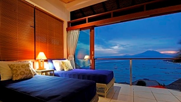 A bedroom with two beds, a nightstand, and a view of the sea and a mountain at dusk. - Lembongan Sanctuary Villas (Lembongan Island)