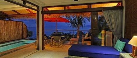 A room with a bed, a ceiling fan, a pool, and a view of the ocean.