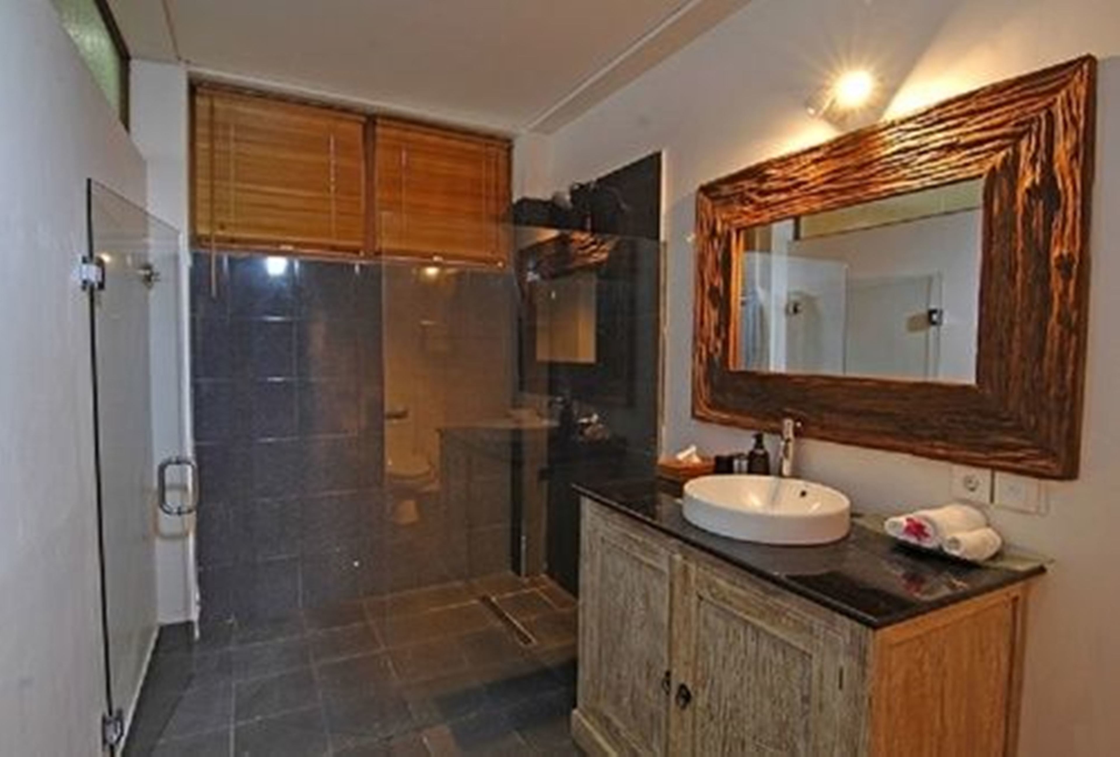 A bathroom with a glass shower enclosure, a wooden cabinet, a sink with a mirror, and a towel on the counter.