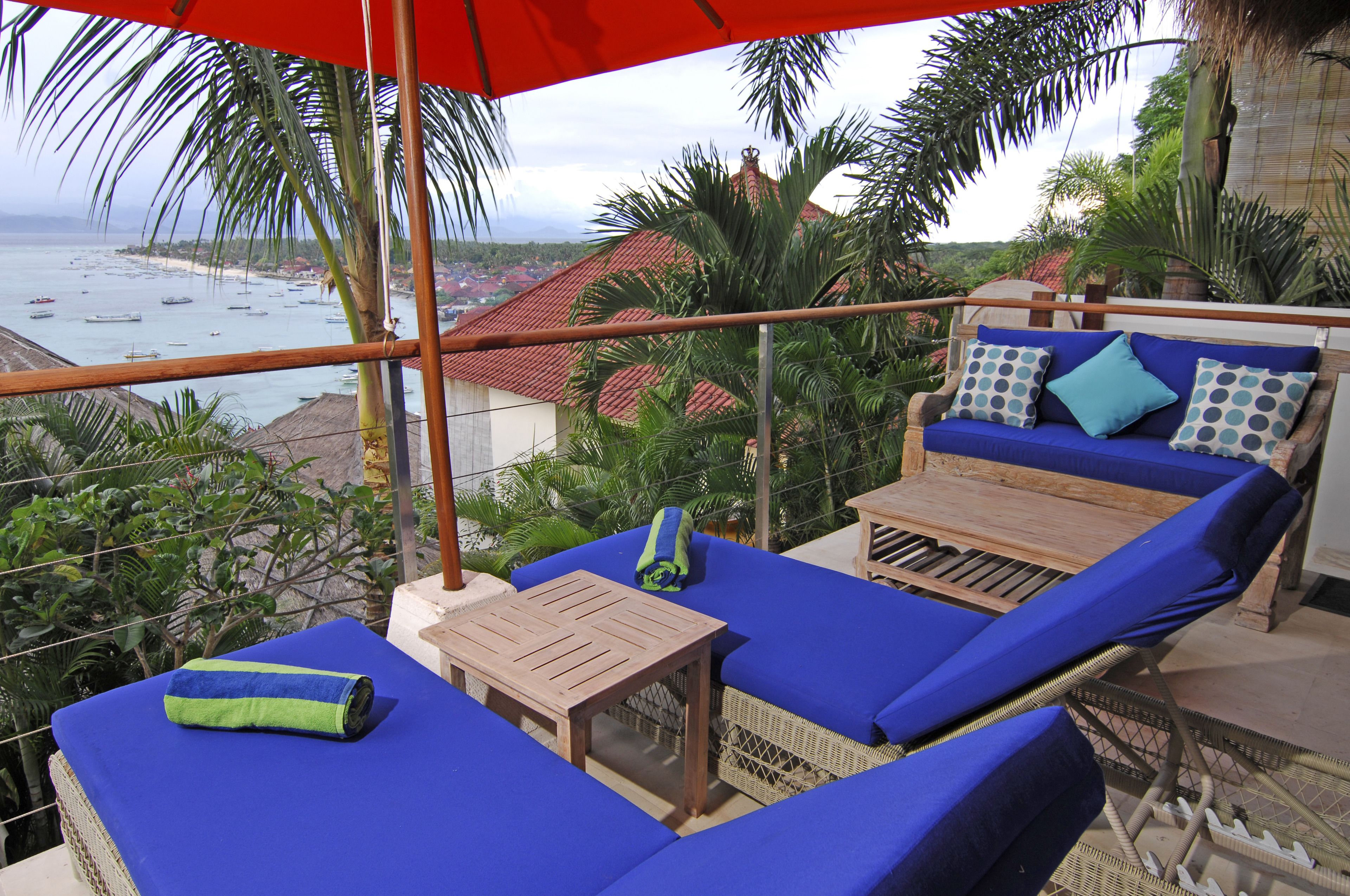 A balcony with blue cushioned seating, a wooden table, and a red umbrella.