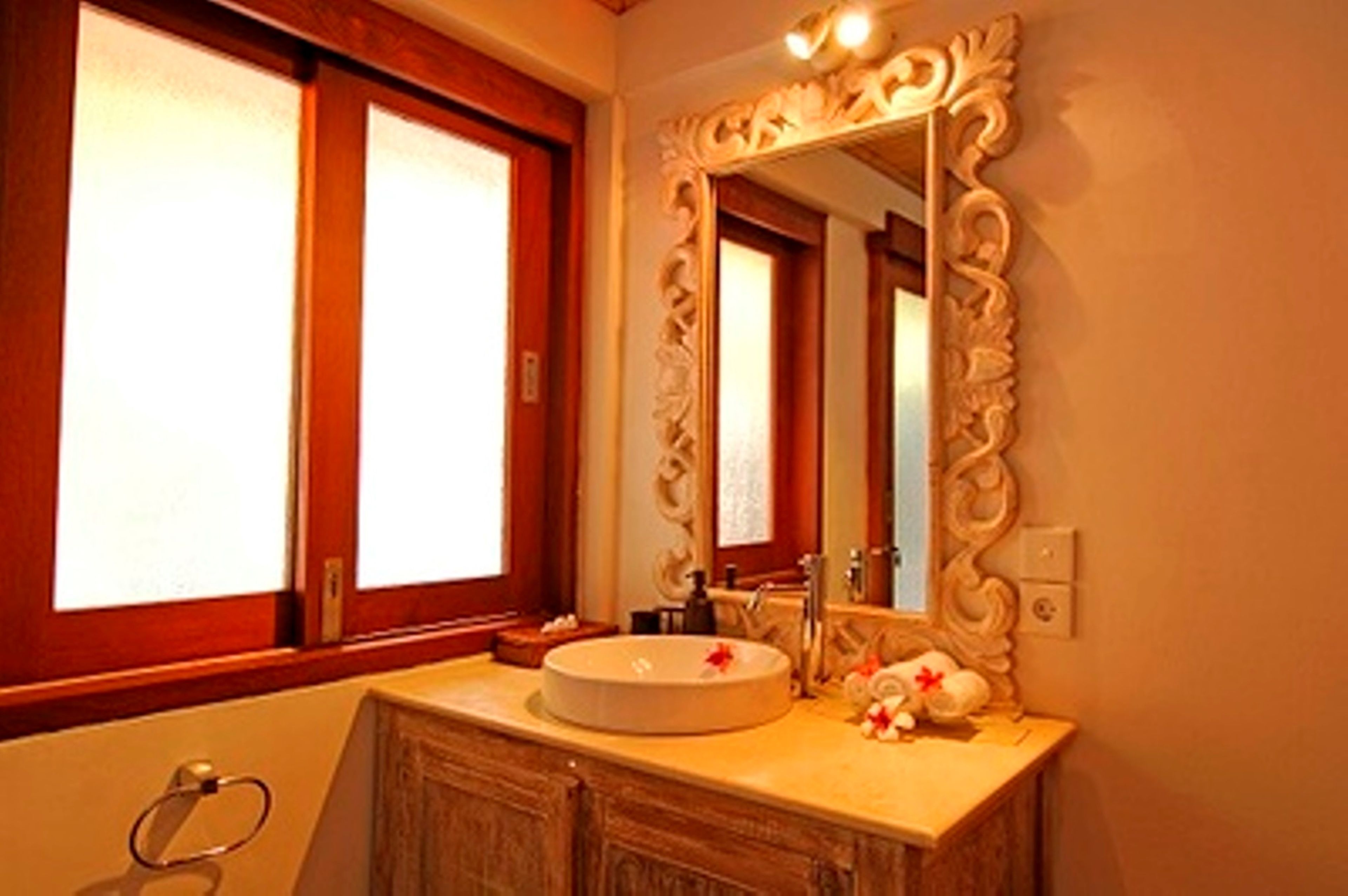 A bathroom with a round sink, a mirror with an ornate frame, and a window with frosted glass.