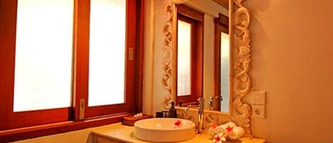 A bathroom with a round sink, a mirror with an ornate frame, and a window with frosted glass.