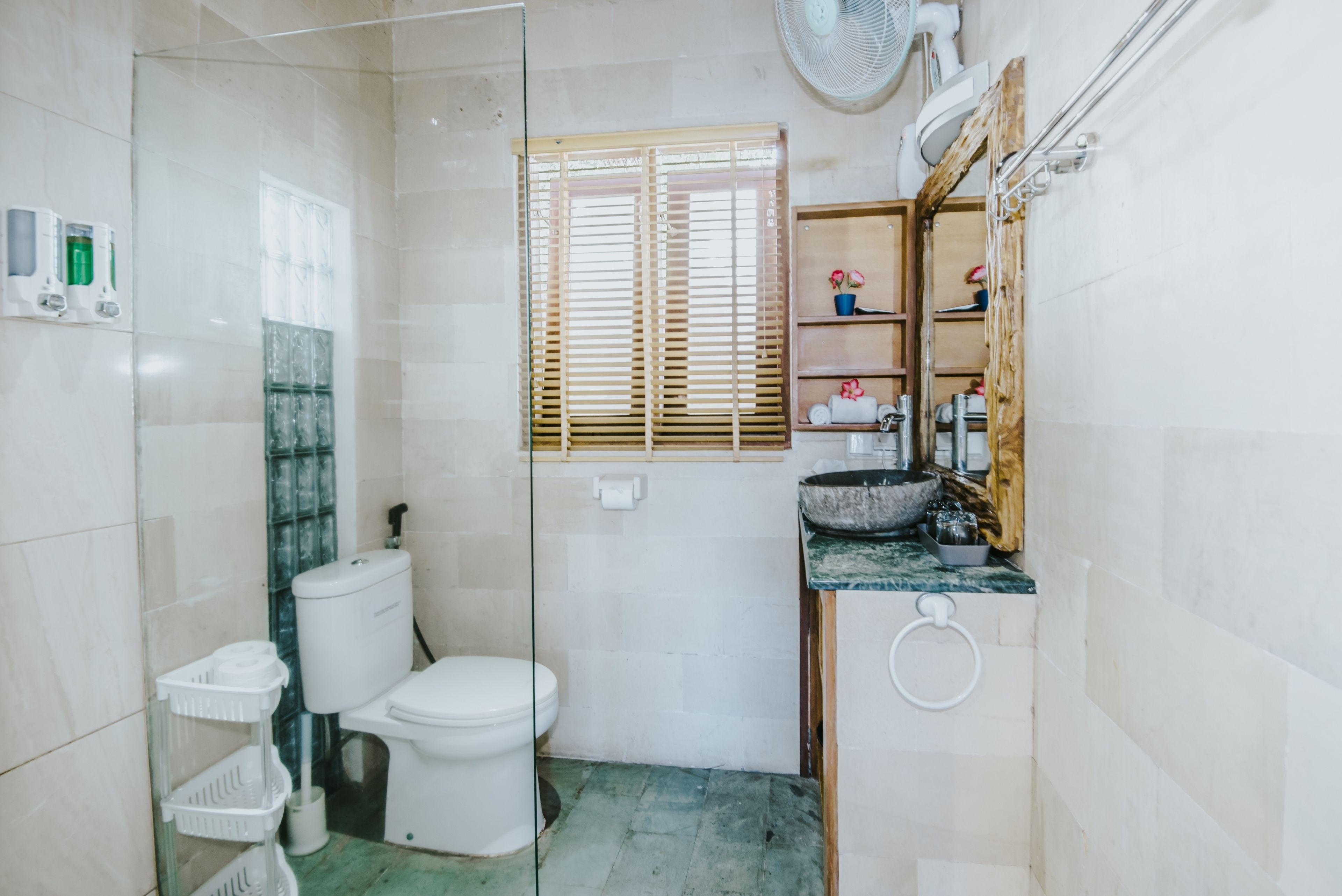 Une petite salle de bain comprenant des toilettes, un lavabo, une douche en verre et une fenêtre avec des stores.